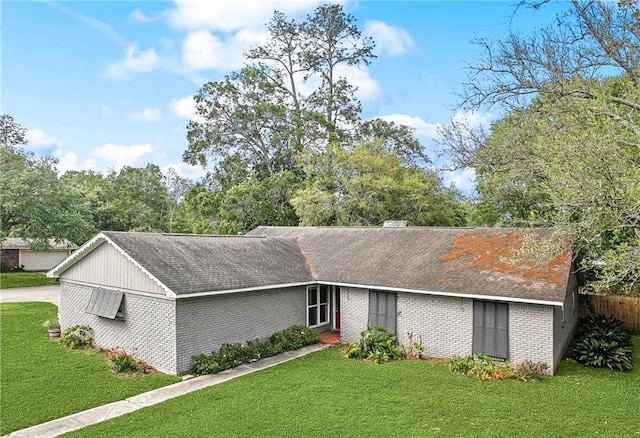 ranch-style home featuring roof with shingles, a front yard, and brick siding