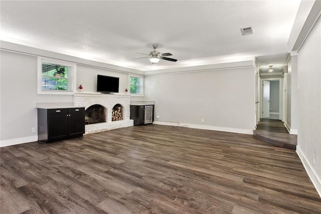unfurnished living room featuring ceiling fan, a brick fireplace, baseboards, dark wood-type flooring, and visible vents