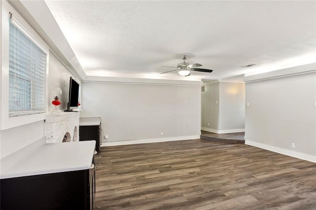 unfurnished living room with ceiling fan, a textured ceiling, a brick fireplace, wood finished floors, and baseboards