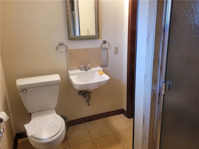 bathroom with toilet, tile patterned floors, baseboards, and a sink