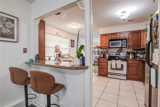 3403 W Loyola Dr, Kenner, LA 70065 - kitchen featuring stainless steel appliances, a kitchen bar, light tile patterned flooring, brown cabinets, and a textured ceiling