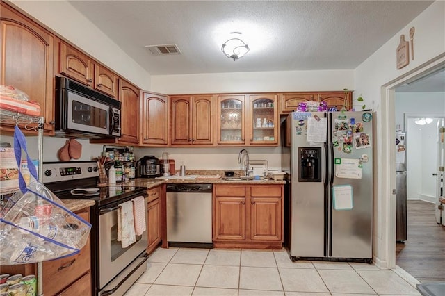 3403 W Loyola Dr, Kenner, LA 70065 - kitchen with stainless steel appliances, a sink, brown cabinetry, glass insert cabinets, and light tile patterned flooring
