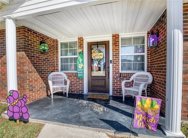 doorway to property featuring a porch and brick siding