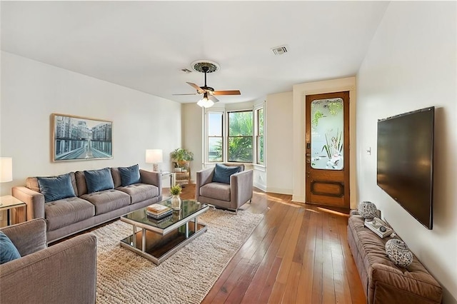 living area featuring baseboards, wood-type flooring, a ceiling fan, and visible vents