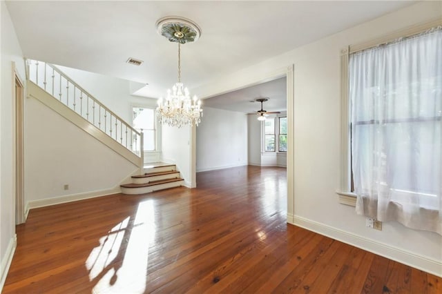 unfurnished dining area featuring ceiling fan with notable chandelier, visible vents, stairway, hardwood / wood-style floors, and baseboards