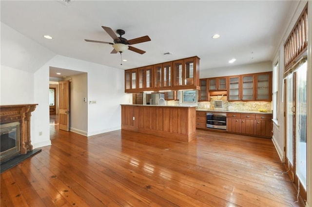 kitchen featuring glass insert cabinets, brown cabinetry, a ceiling fan, appliances with stainless steel finishes, and light wood finished floors