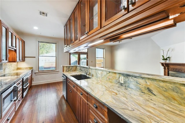 kitchen with a sink, baseboards, light stone counters, and brown cabinets