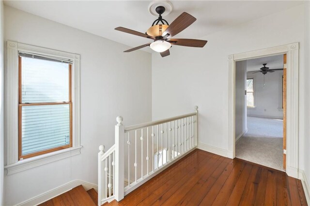 corridor with an upstairs landing, wood-type flooring, and baseboards
