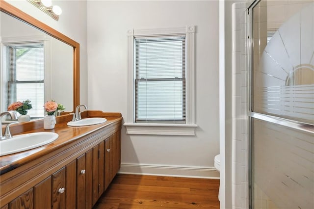 bathroom featuring a shower with shower door, baseboards, a sink, and wood finished floors