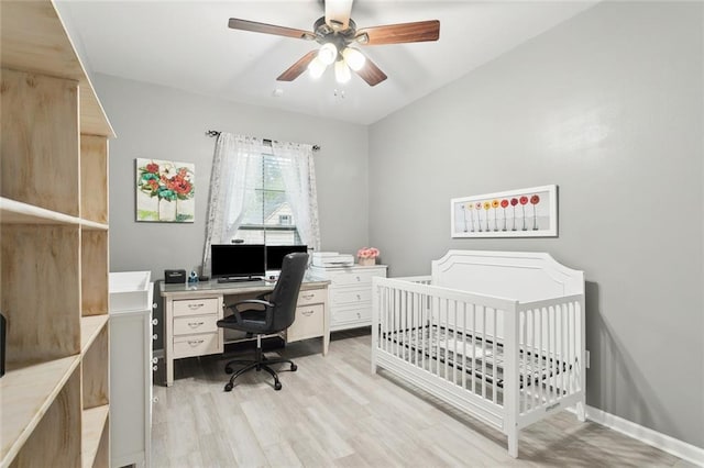 bedroom featuring a nursery area, baseboards, light wood-type flooring, and a ceiling fan