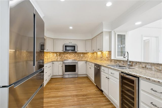 kitchen with light stone counters, a sink, light wood-style flooring, stainless steel appliances, and wine cooler