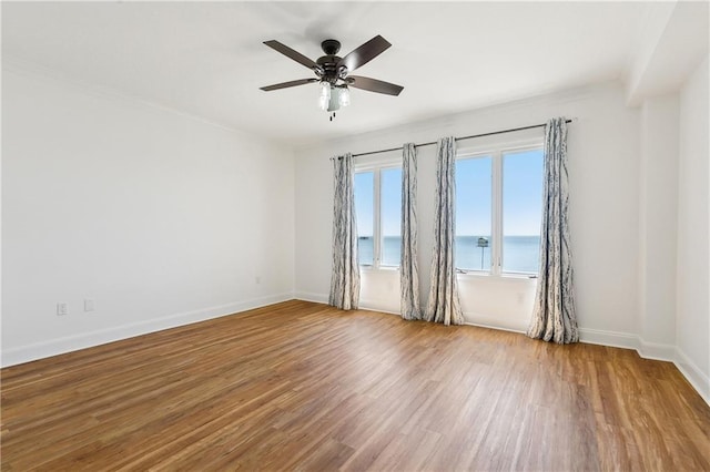 unfurnished room with baseboards, ceiling fan, a water view, and wood finished floors