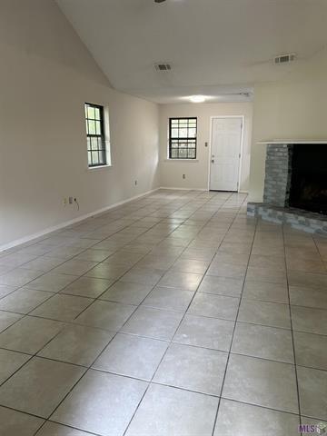 spare room with baseboards, a brick fireplace, and light tile patterned floors