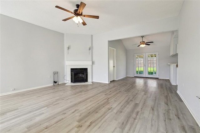 unfurnished living room featuring light wood-type flooring, a ceiling fan, vaulted ceiling, a tiled fireplace, and french doors