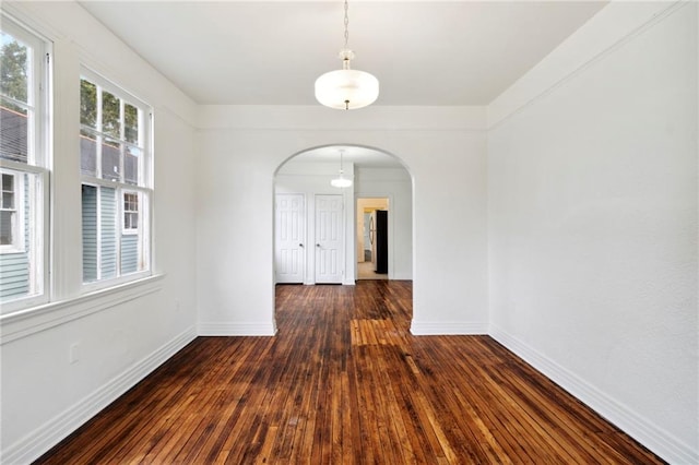 unfurnished dining area featuring arched walkways, baseboards, and hardwood / wood-style floors