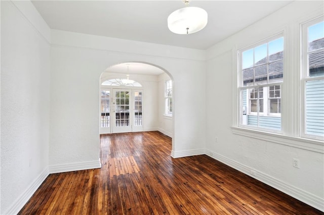 unfurnished room featuring arched walkways, baseboards, and dark wood finished floors