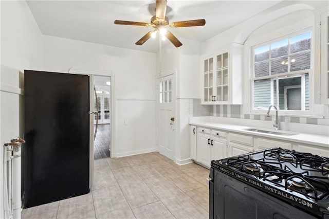 kitchen featuring black gas range oven, a sink, a ceiling fan, white cabinetry, and glass insert cabinets