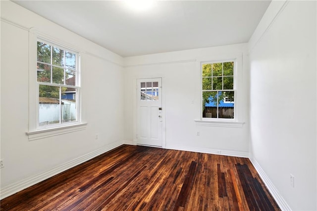 empty room with dark wood-style flooring, baseboards, and a healthy amount of sunlight