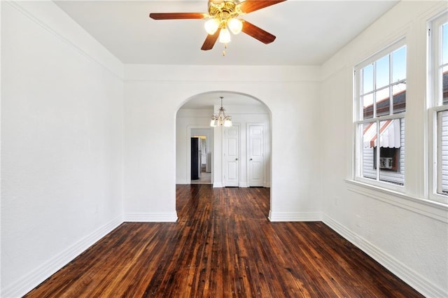 spare room with arched walkways, baseboards, ceiling fan with notable chandelier, and dark wood-type flooring