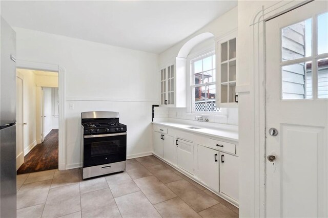 kitchen with gas range, light countertops, light tile patterned floors, white cabinets, and glass insert cabinets