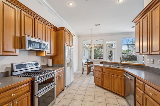 kitchen with a sink, stainless steel appliances, a notable chandelier, brown cabinetry, and dark countertops