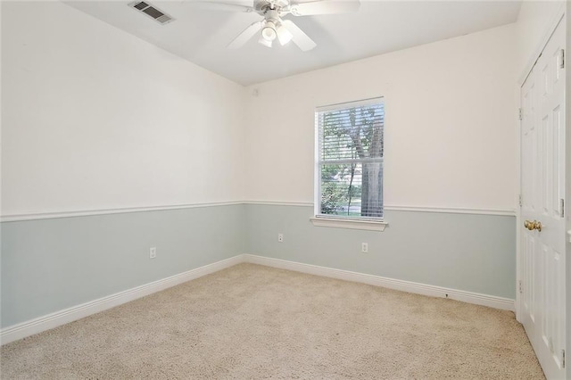 spare room featuring light colored carpet, visible vents, ceiling fan, and baseboards