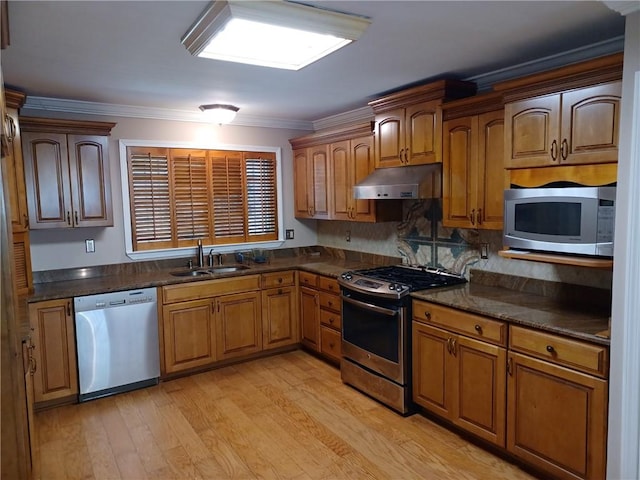 kitchen with crown molding, appliances with stainless steel finishes, under cabinet range hood, dark countertops, and a sink