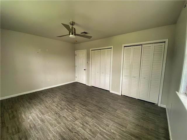 2359 Prentiss Ave, New Orleans, LA 70122 - unfurnished bedroom with dark wood-style flooring, baseboards, a ceiling fan, and two closets