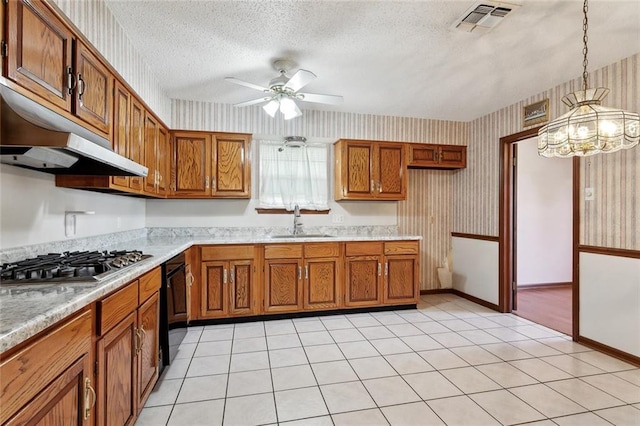 kitchen featuring stainless steel gas cooktop, brown cabinets, a sink, under cabinet range hood, and wallpapered walls