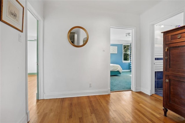 corridor with light wood-type flooring and baseboards