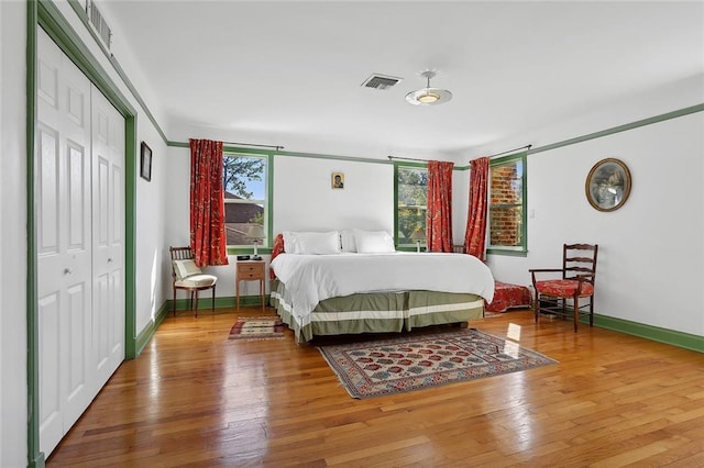 bedroom with baseboards, visible vents, hardwood / wood-style flooring, and multiple windows