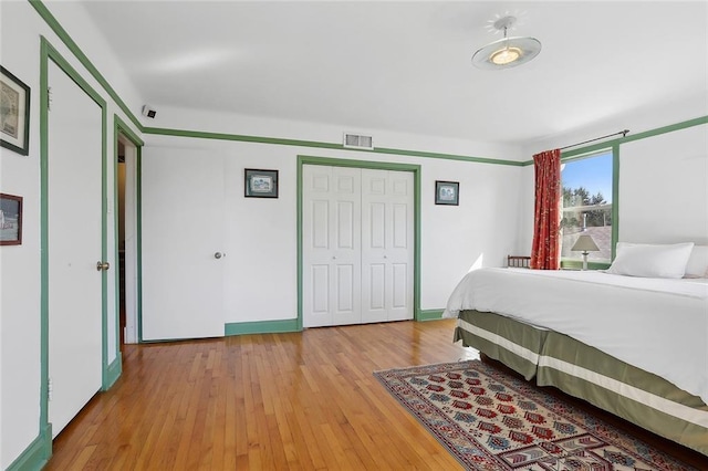 bedroom with baseboards, light wood finished floors, visible vents, and a closet