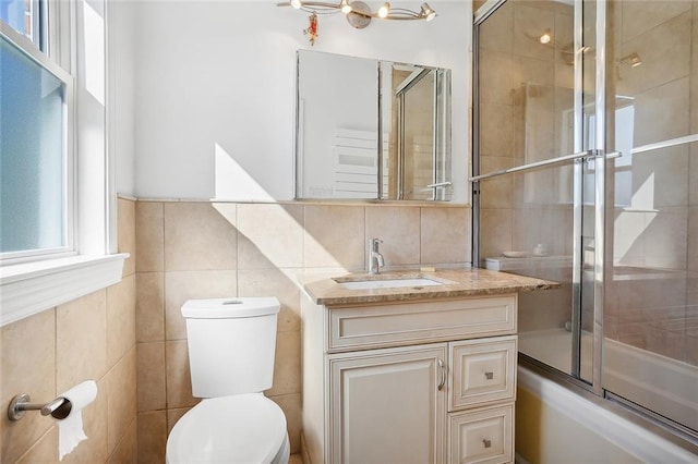 bathroom featuring tile walls, vanity, enclosed tub / shower combo, and toilet