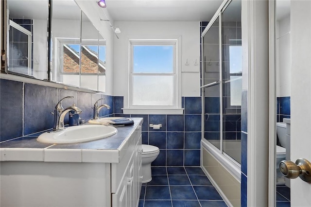 full bath featuring tile patterned floors, vanity, tile walls, toilet, and shower / bath combination with glass door