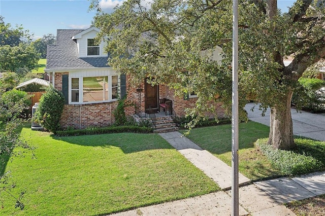 view of front facade with a shingled roof, brick siding, and a front yard