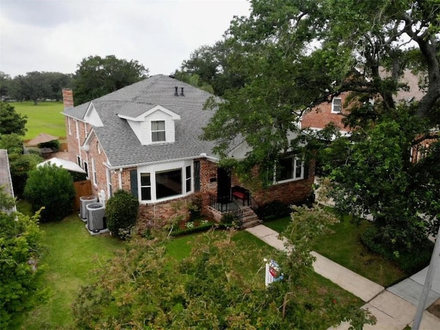 view of front facade with brick siding, a front yard, central AC, and a chimney
