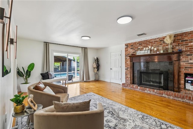 living room featuring a fireplace, visible vents, baseboards, and wood finished floors
