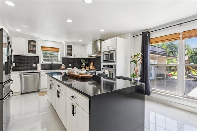 kitchen with tasteful backsplash, wall chimney exhaust hood, light tile patterned flooring, and appliances with stainless steel finishes