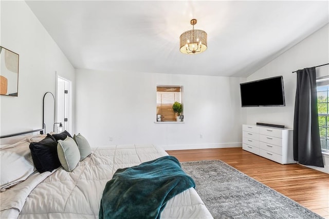 bedroom with baseboards, vaulted ceiling, a notable chandelier, and wood finished floors