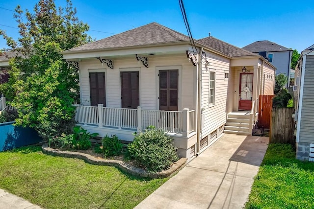 view of front of home with a porch, a shingled roof, a front lawn, and fence