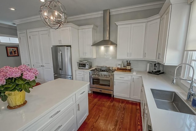 kitchen with wall chimney range hood, white cabinetry, crown molding, appliances with stainless steel finishes, and a sink