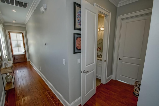 corridor with ornamental molding, visible vents, baseboards, and wood finished floors