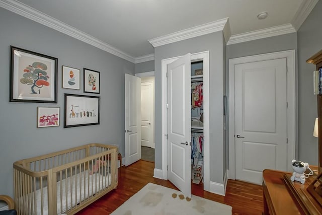 bedroom featuring a closet, baseboards, ornamental molding, a nursery area, and wood finished floors
