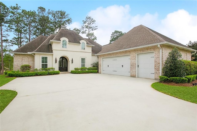 french provincial home with a garage, brick siding, driveway, and a shingled roof