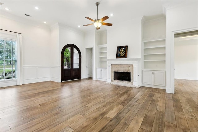 unfurnished living room with wood finished floors, ceiling fan, built in shelves, and visible vents