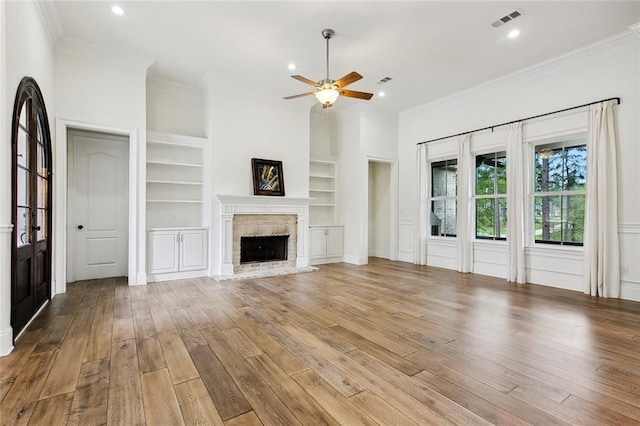 unfurnished living room featuring a ceiling fan, crown molding, visible vents, built in shelves, and wood finished floors