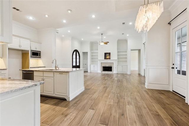 kitchen featuring ceiling fan with notable chandelier, white cabinets, a sink, stainless steel appliances, and light wood finished floors