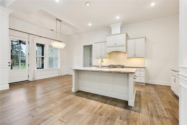 kitchen featuring a sink, light wood finished floors, a kitchen island with sink, and white cabinetry