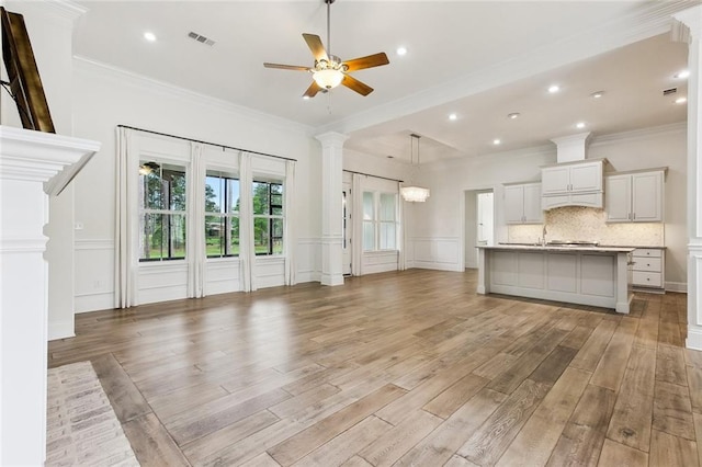 unfurnished living room with light wood-type flooring, a decorative wall, ceiling fan, and ornamental molding