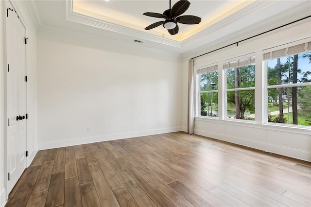 spare room featuring wood finished floors, baseboards, crown molding, and a raised ceiling